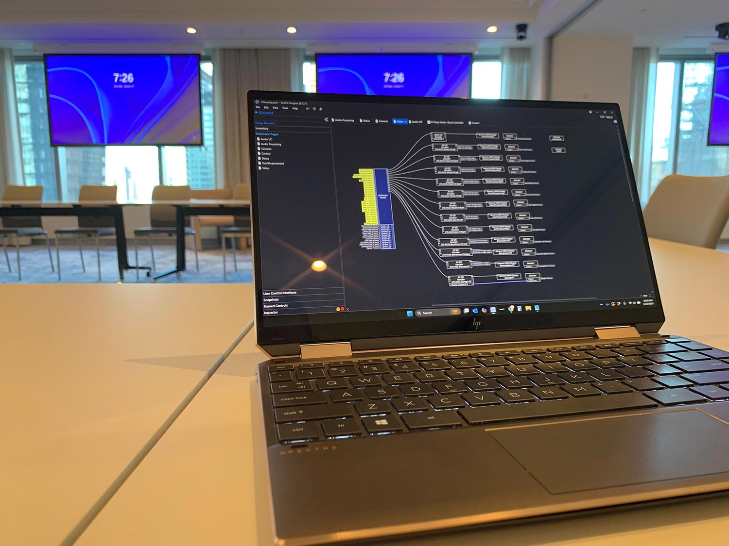 Laptop displaying an AV system configuration in a modern conference room with large screens