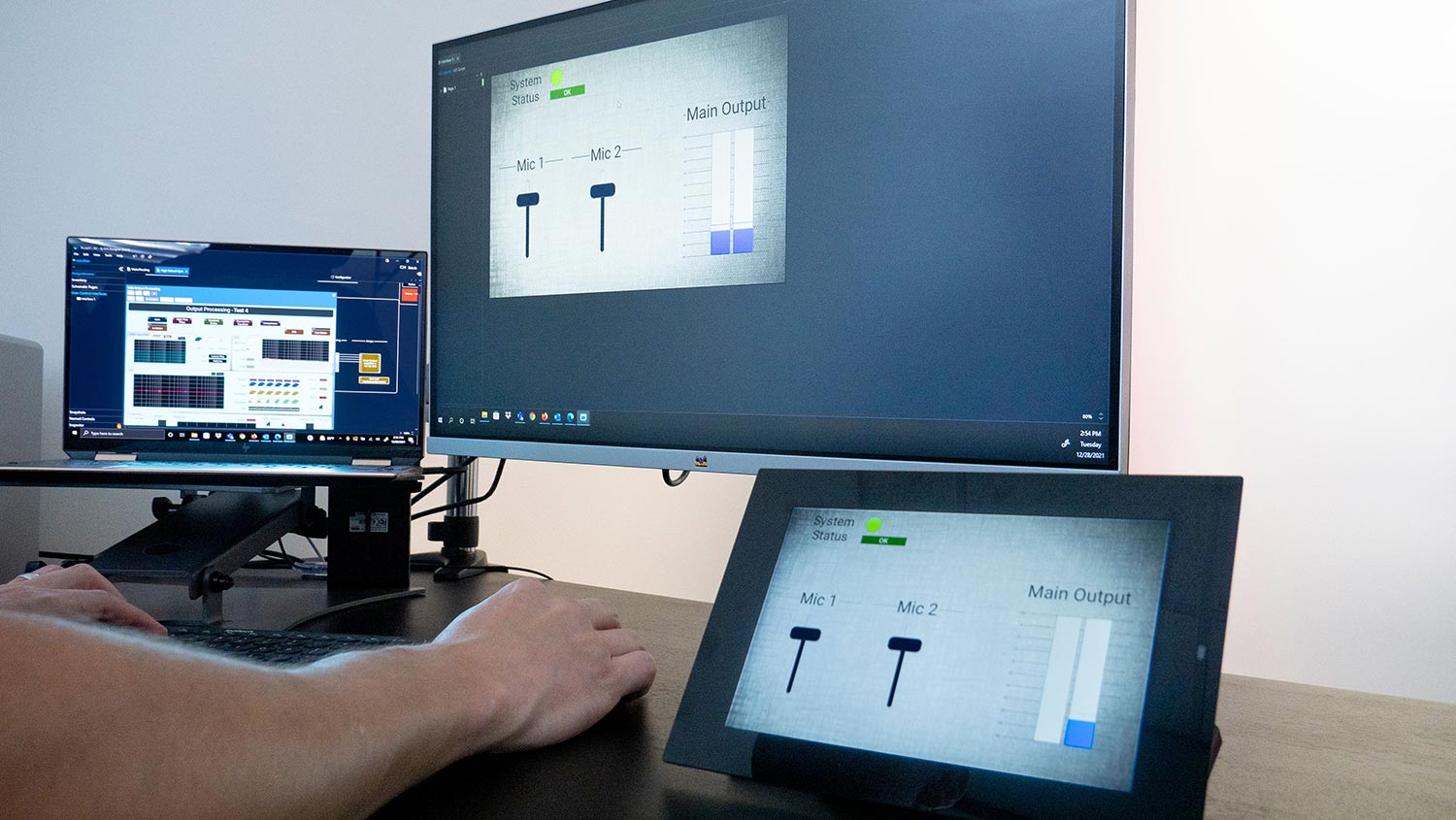 AV control system displayed on a touchscreen, monitor, and laptop at a workstation