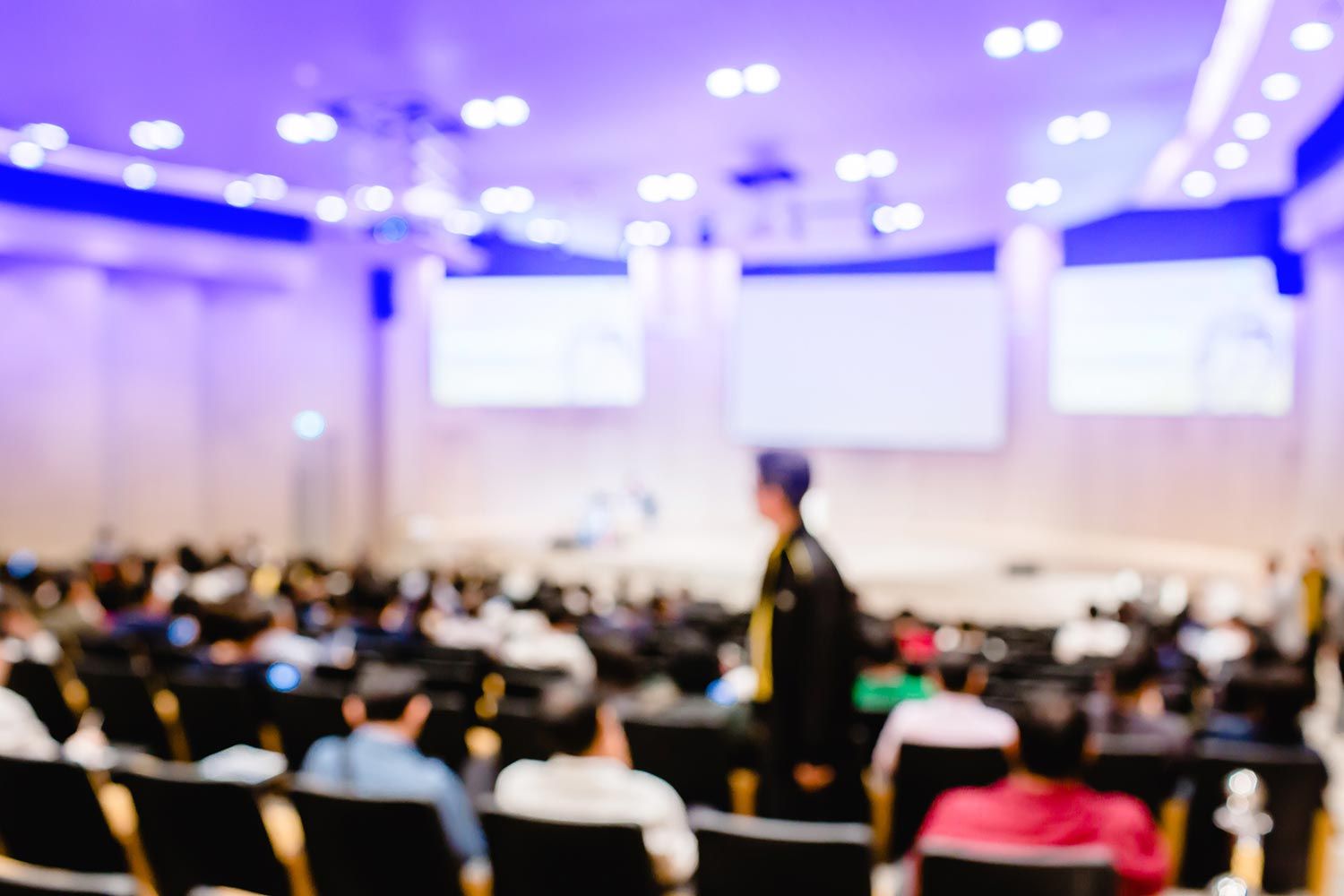 Blurry view of a conference hall filled with attendees and bright lighting